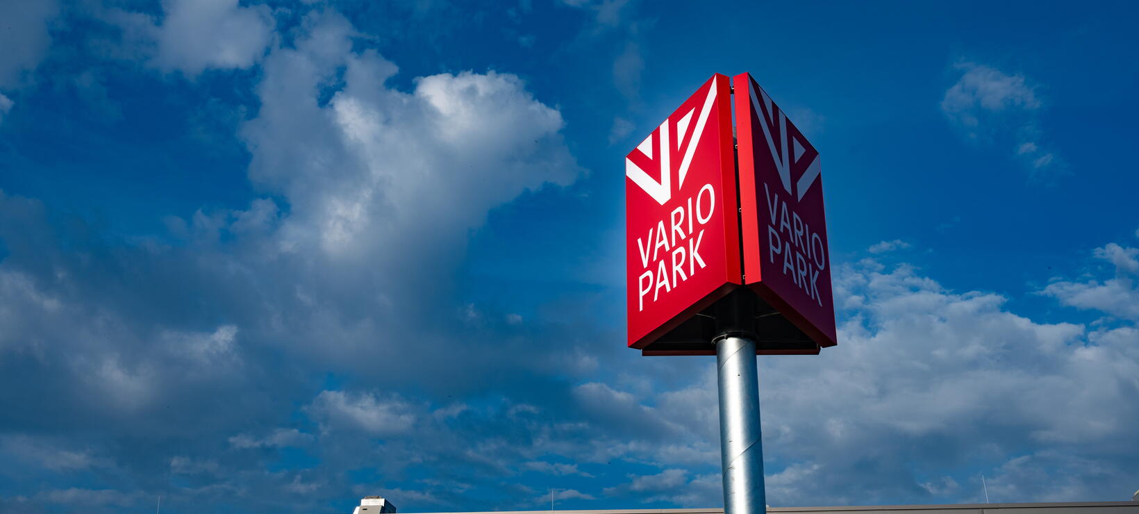 Werbepylon mit dem Logg der VarioPark vor blauem Himmel und einer Teilansicht des Gebäudes